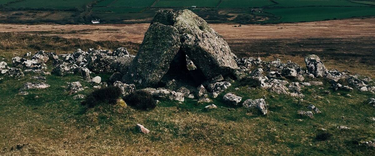 A stone cairn surrounded by rocks in a grassy field with rolling hills in the background.