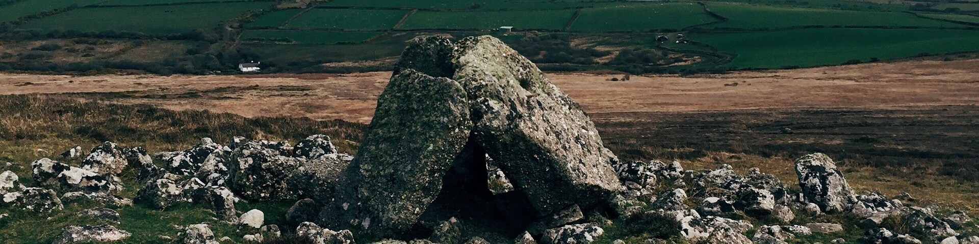 A stone cairn surrounded by rocks in a grassy field with rolling hills in the background.