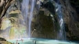 A waterfall cascading into a clear pool surrounded by rocky cliffs and bamboo.