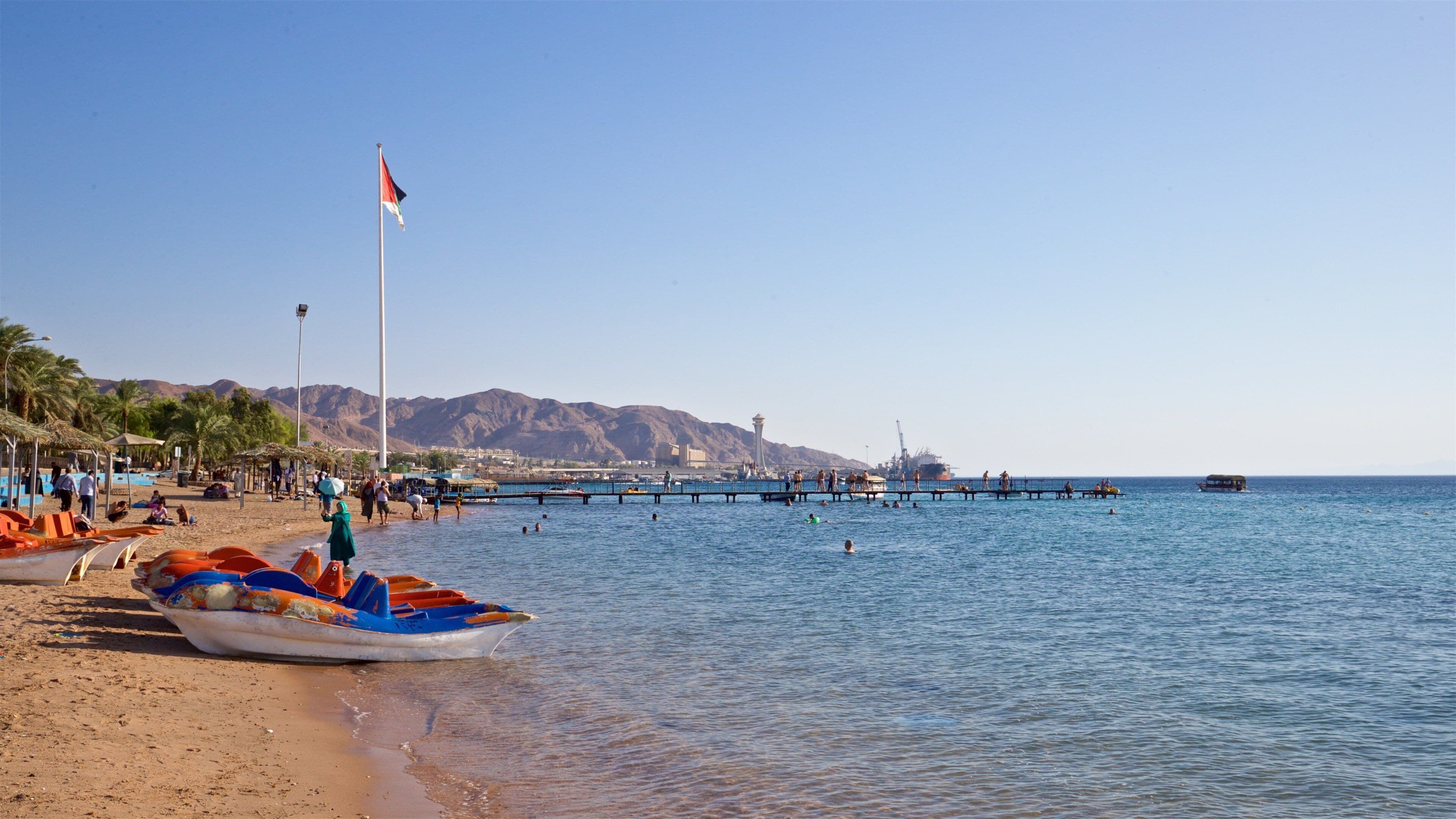 A beach with boats, a pier, and mountains in the background.