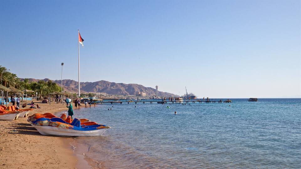 A beach with boats, a pier, and mountains in the background.