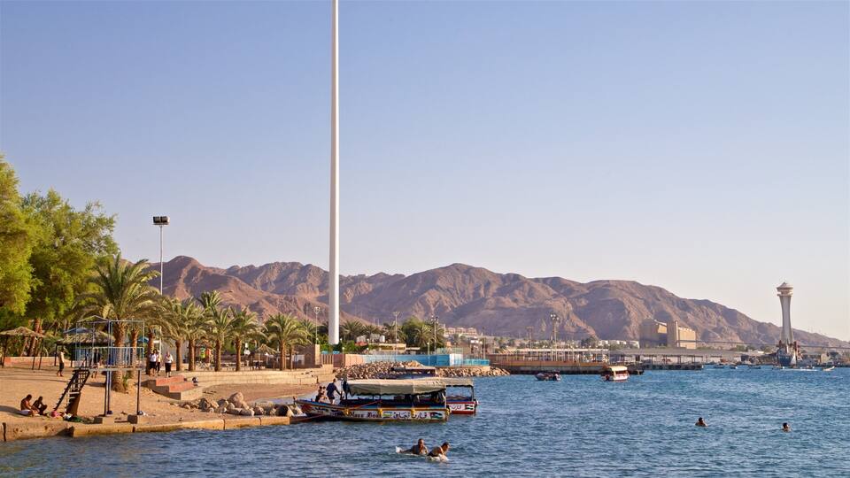 A coastal city with boats, a lighthouse, and mountains in the background.