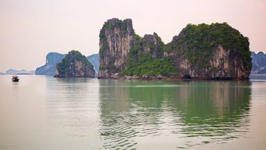 Mar calmo com um barco e uma grande ilha de calcário coberta por vegetação densa e verde.