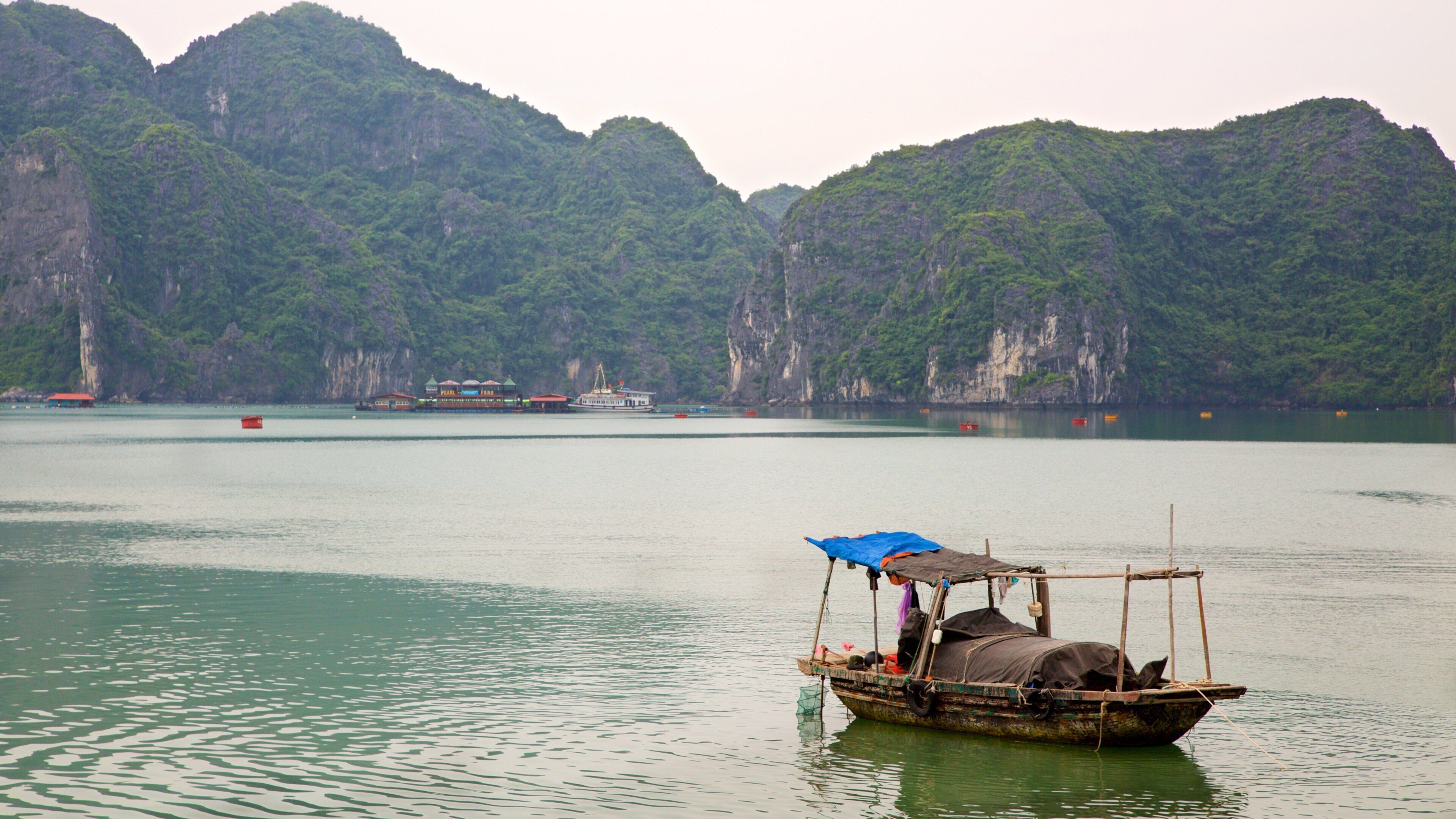 A traditional boat with a blue tarp on calm water surrounded by lush green mountains.