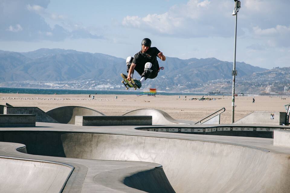 Un skateur effectuant une figure dans un skatepark, avec des montagnes en arrière-plan.