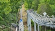A roller coaster track in a forested area with a steep incline and a bridge structure.