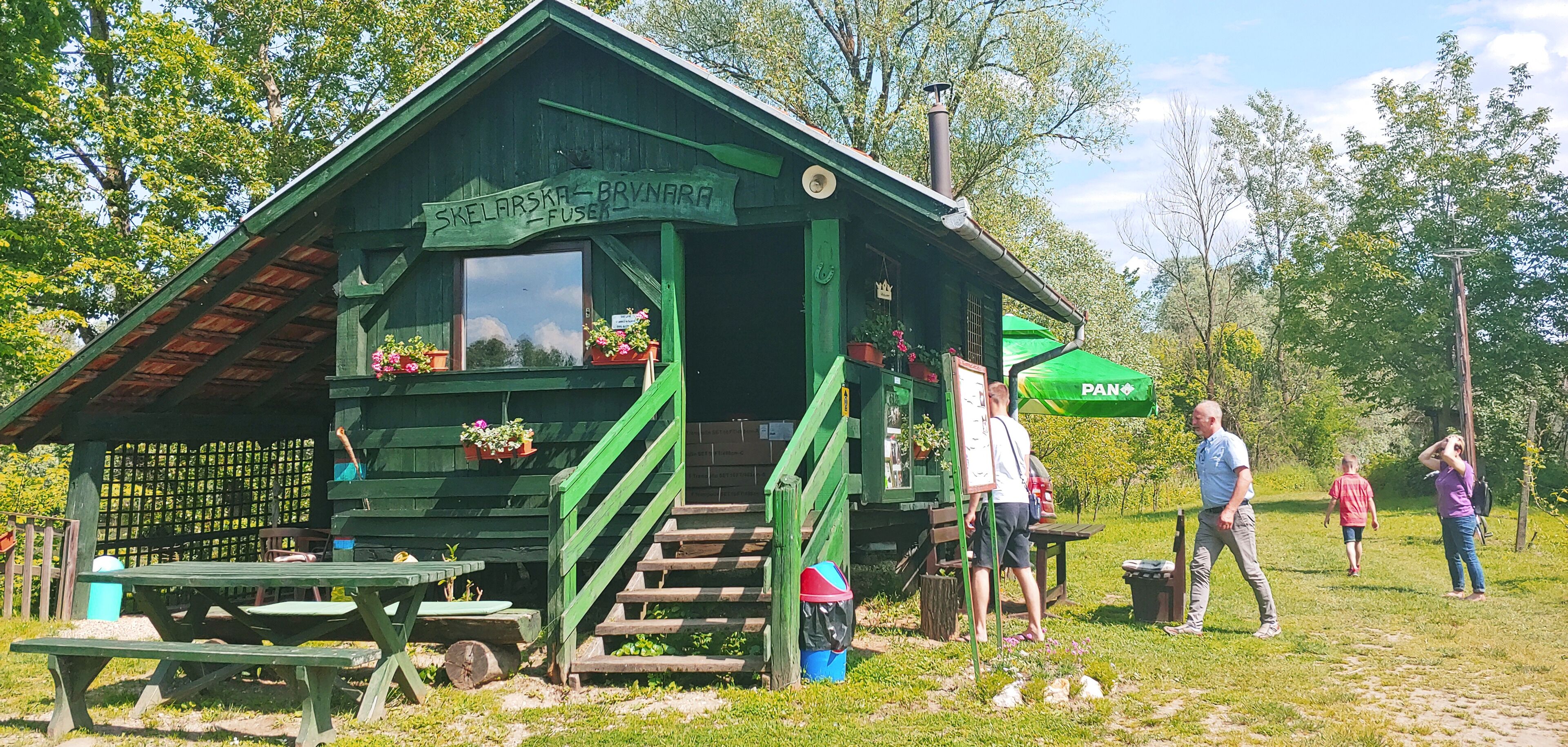 A green wooden cabin with a sign reading "Skelarska - Brynara" and a green umbrella.