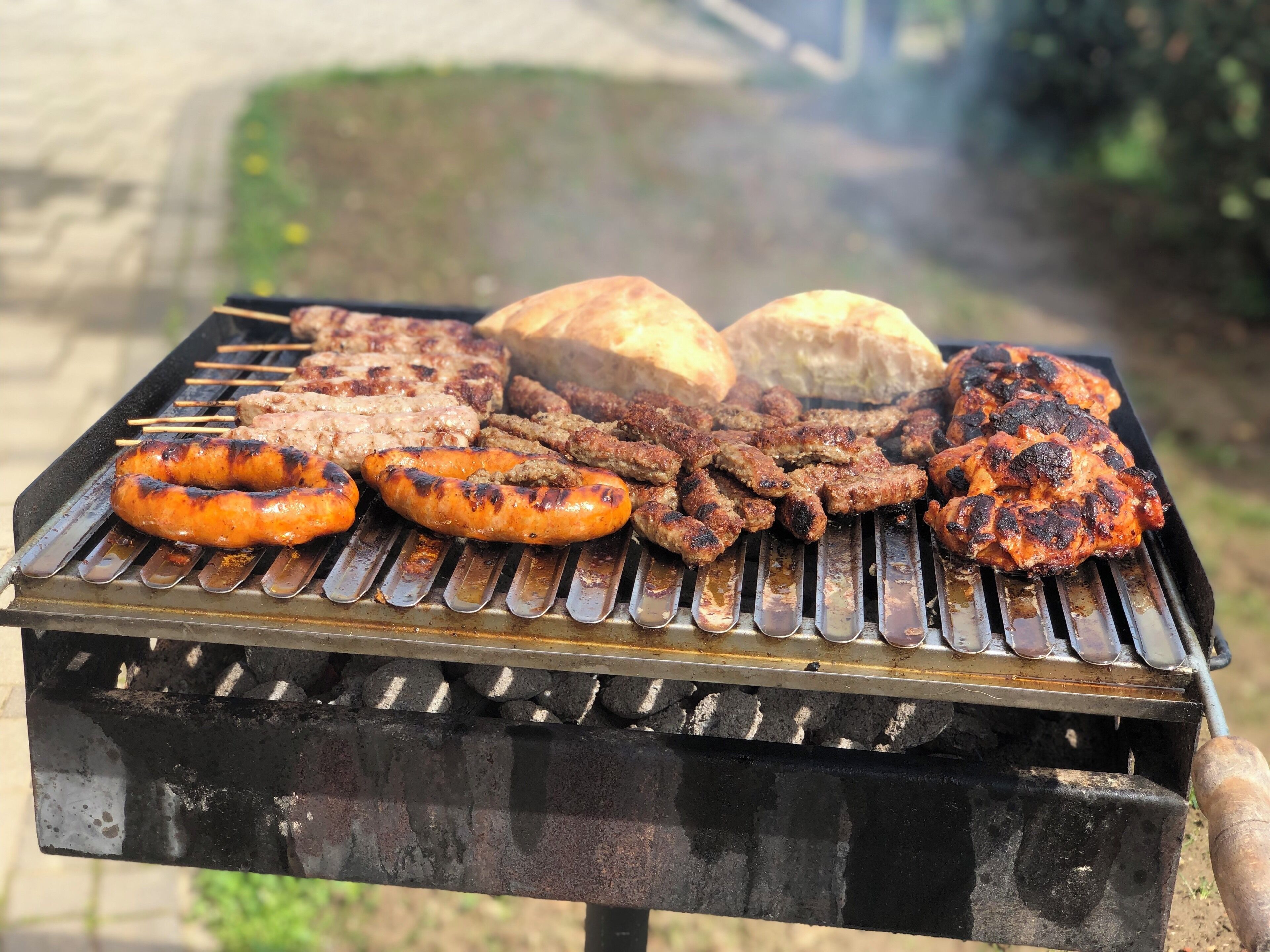 A barbecue grill with sausages, skewers, and bread.