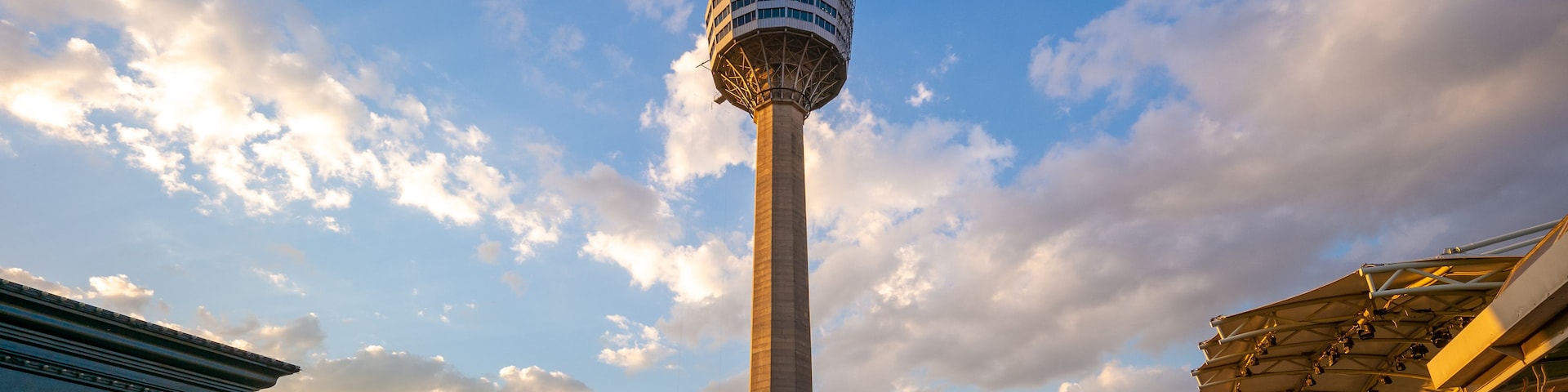 Una torre con una plataforma de observación esférica, rodeada de zonas de estar al aire libre y un autobús rojo.