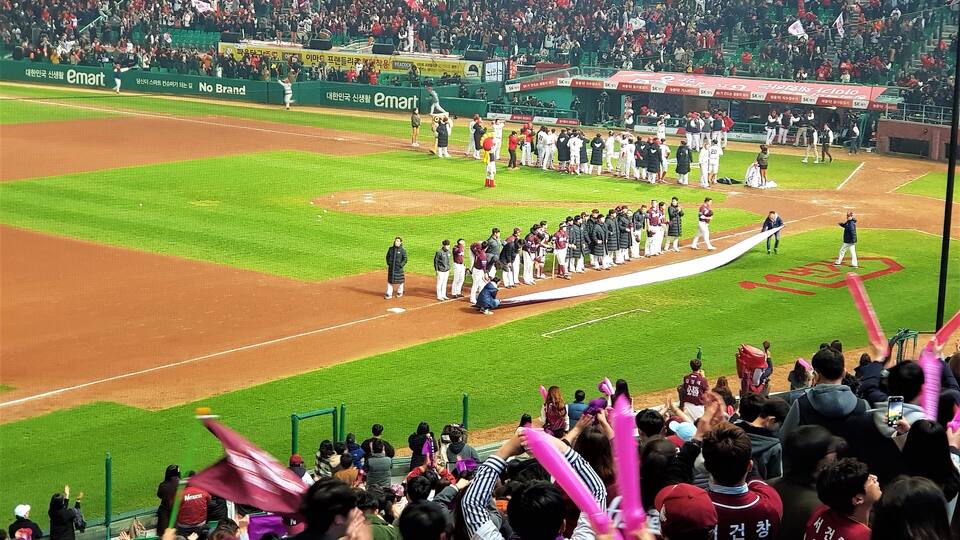 A baseball field with a crowd of spectators and players lined up for a ceremony.