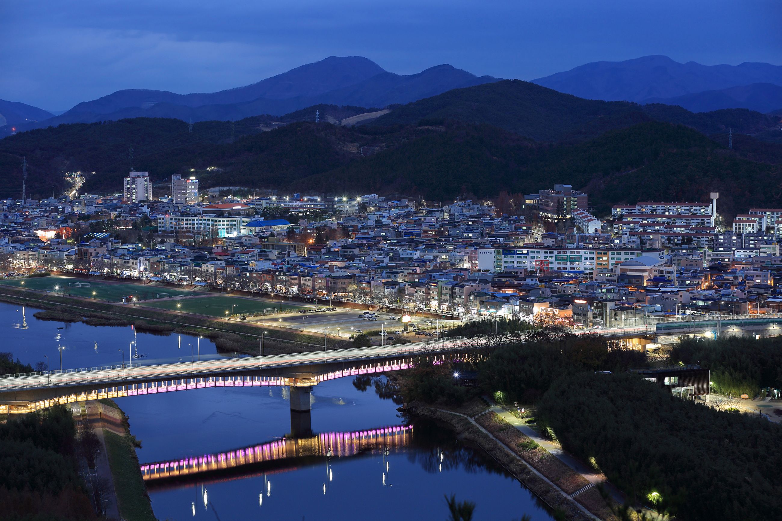 Jung-gu, Ulsan, South Korea - December 12, 2022: High angle and night view of National Garden Bridge on Taehwa River against houses and apartments in the background
