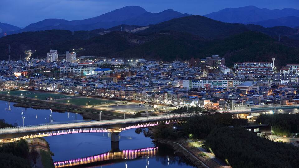 Jung-gu, Ulsan, South Korea - December 12, 2022: High angle and night view of National Garden Bridge on Taehwa River against houses and apartments in the background