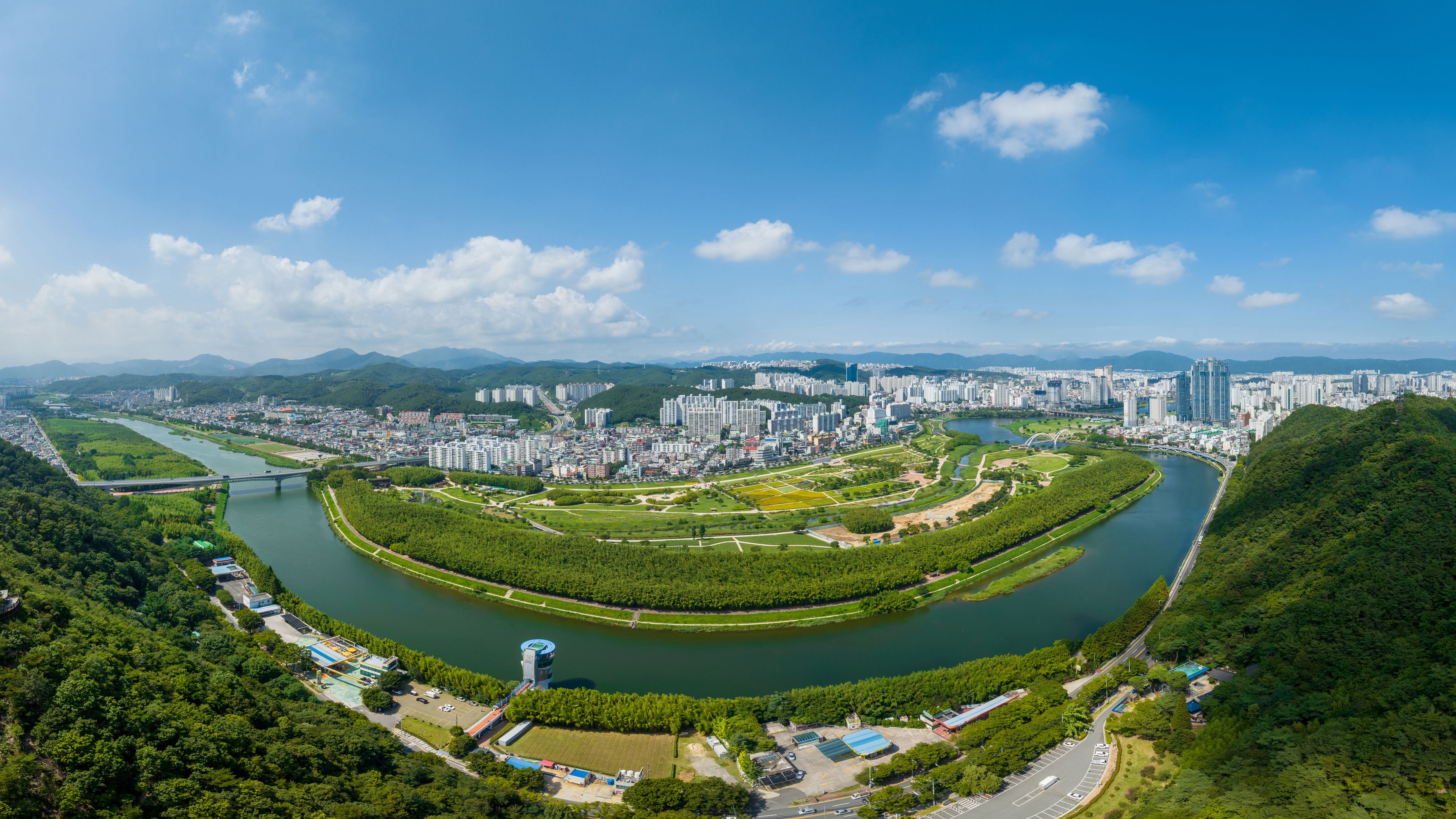 Taehwa-dong, Jung-gu, Ulsan, South Korea - July 30, 2022: Aerial and panoramic view of Sibli Pine Forest and Taehwagang National Garden near Taehwa River aginst apartments in summer