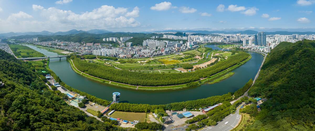 Taehwa-dong, Jung-gu, Ulsan, South Korea - July 30, 2022: Aerial and panoramic view of Sibli Pine Forest and Taehwagang National Garden near Taehwa River aginst apartments in summer