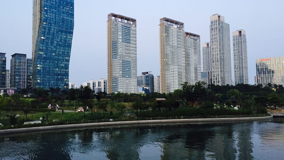 A cityscape with modern skyscrapers and a calm body of water reflecting the buildings.
