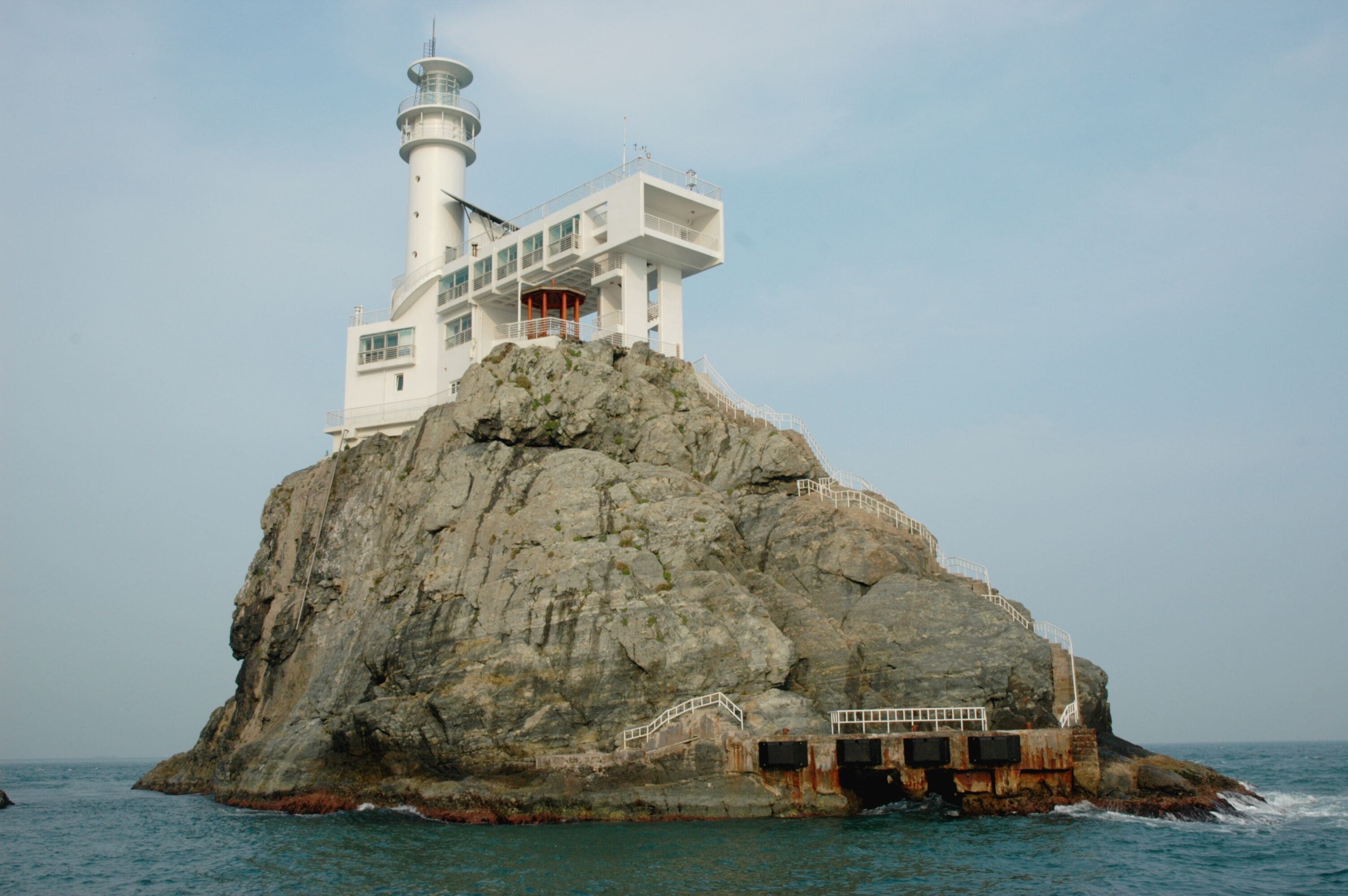 A lighthouse on a rocky outcrop with a white building on top, surrounded by the sea.