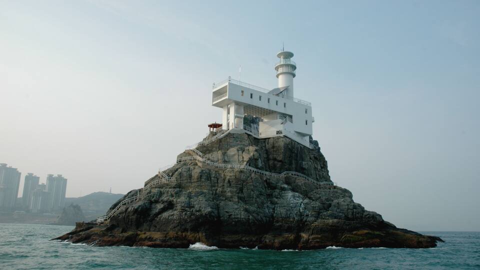 A lighthouse on a rocky island with a clear sky.