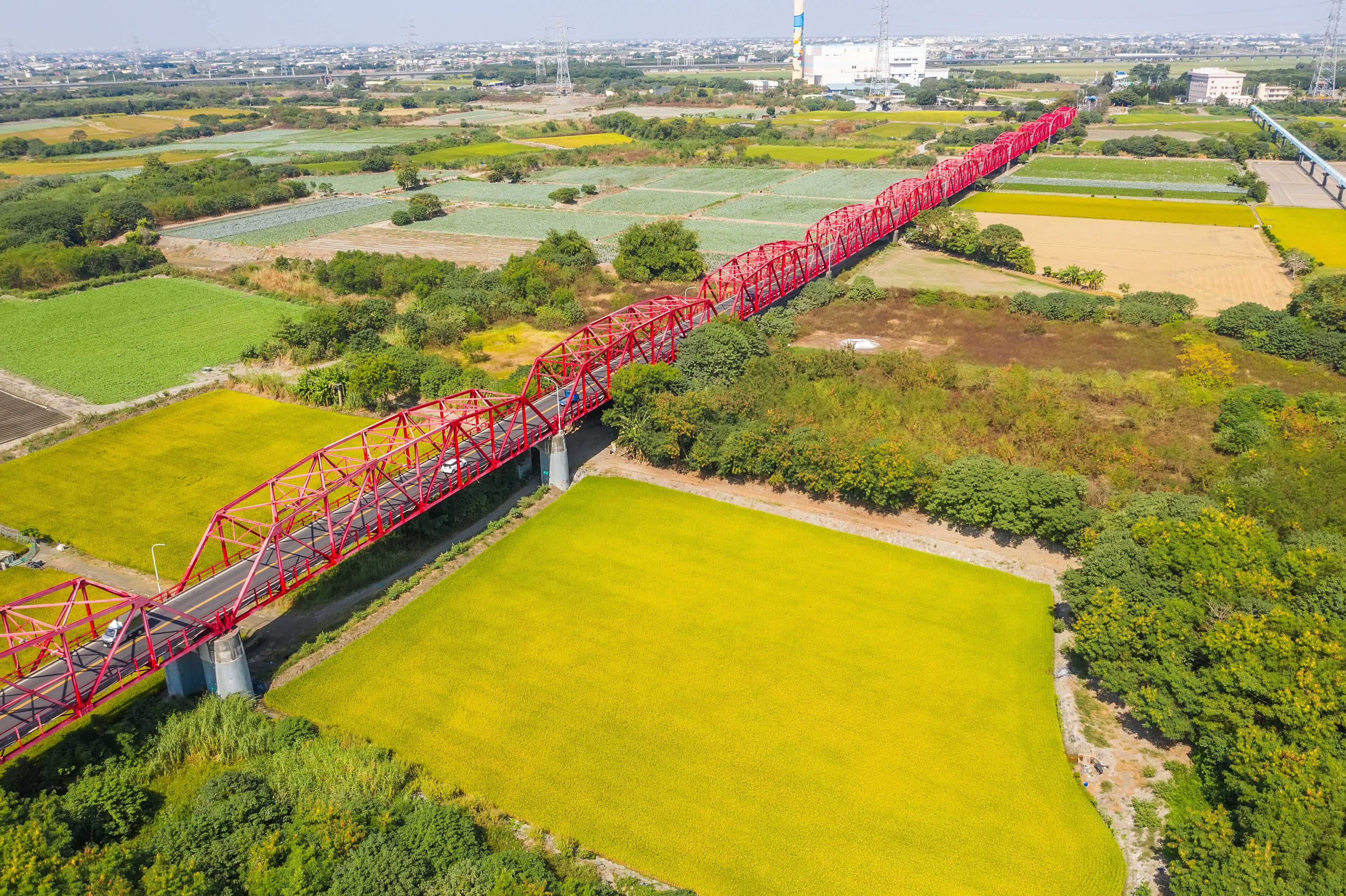A red bridge spanning a river over agricultural fields.