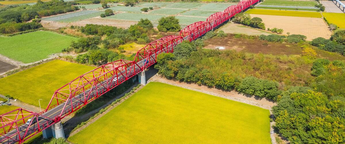 A red bridge spanning a river over agricultural fields.
