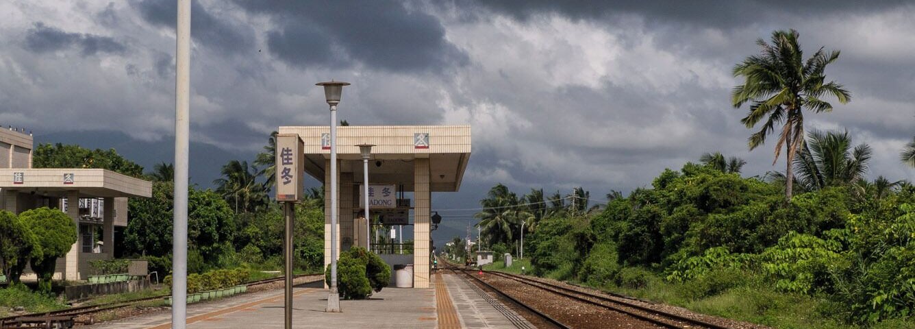 Plataforma de estação de trem com abrigo, poste de luz e trilhos.