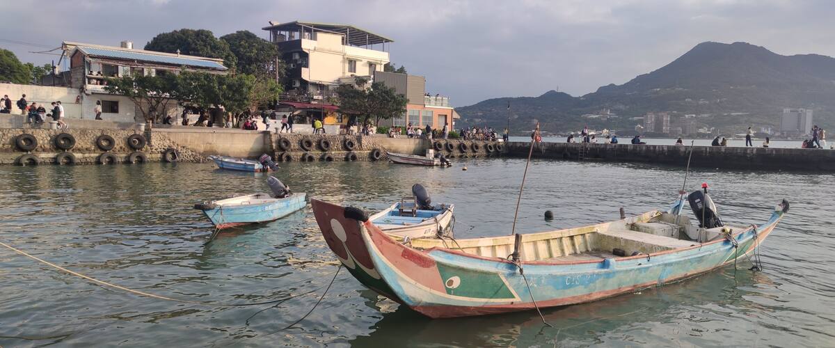 A harbor with boats, a stone wall with tires, and buildings in the background.