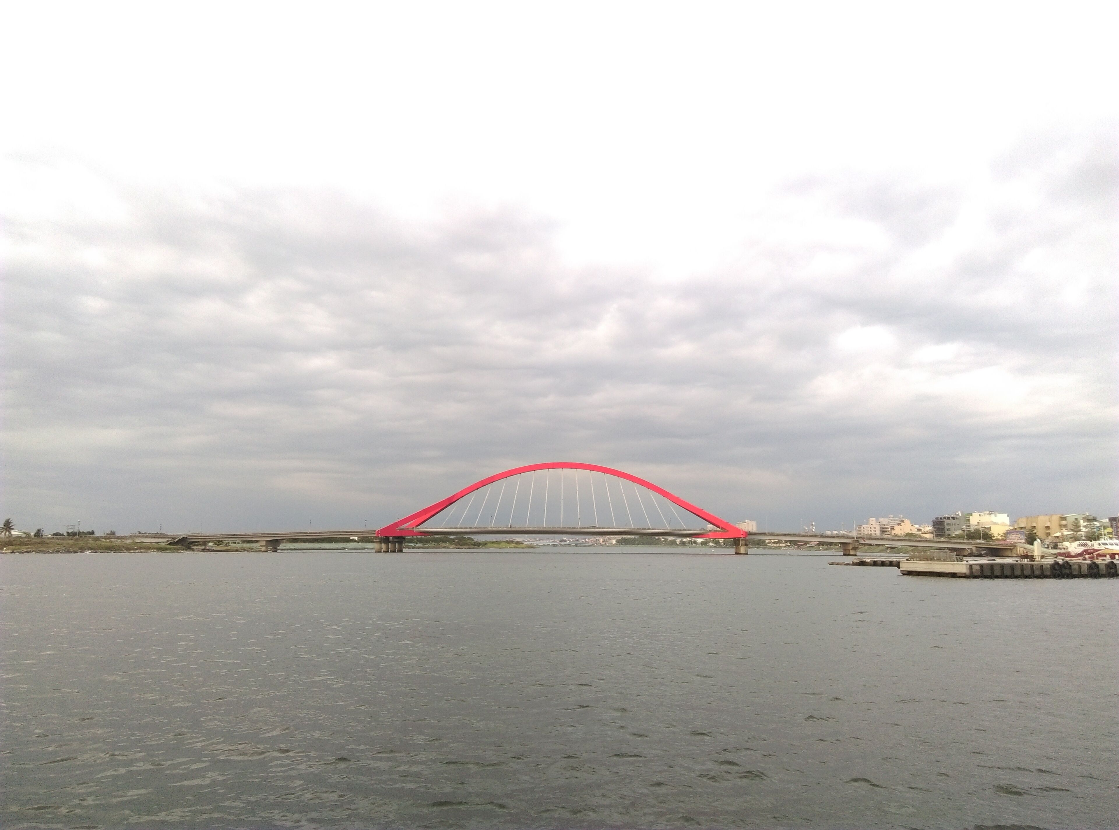 A red bridge over a body of water with a cloudy sky.