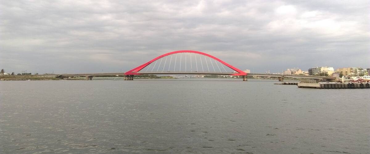 A red bridge over a body of water with a cloudy sky.