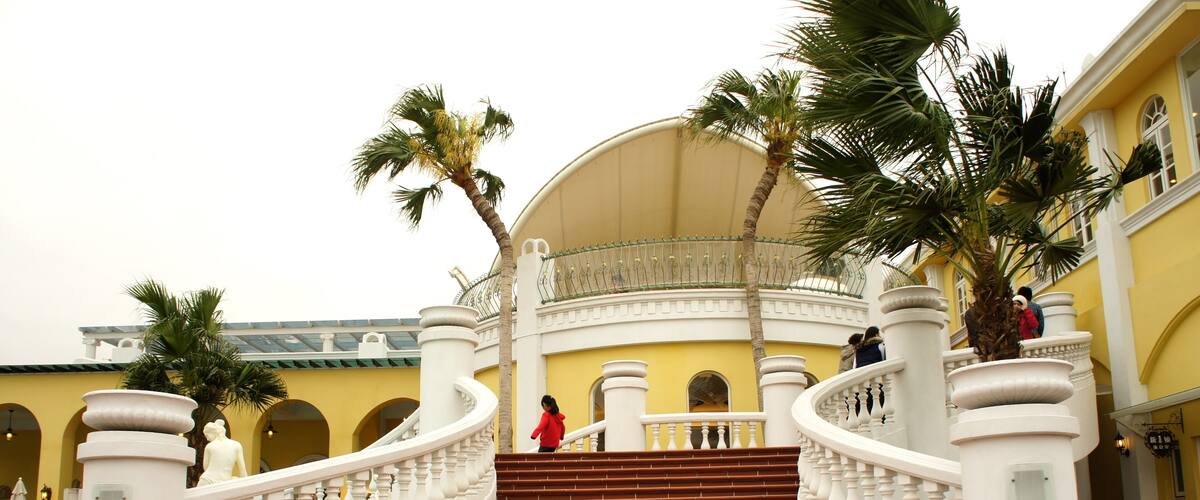 A grand staircase with white balustrades, palm trees, and a yellow building facade.