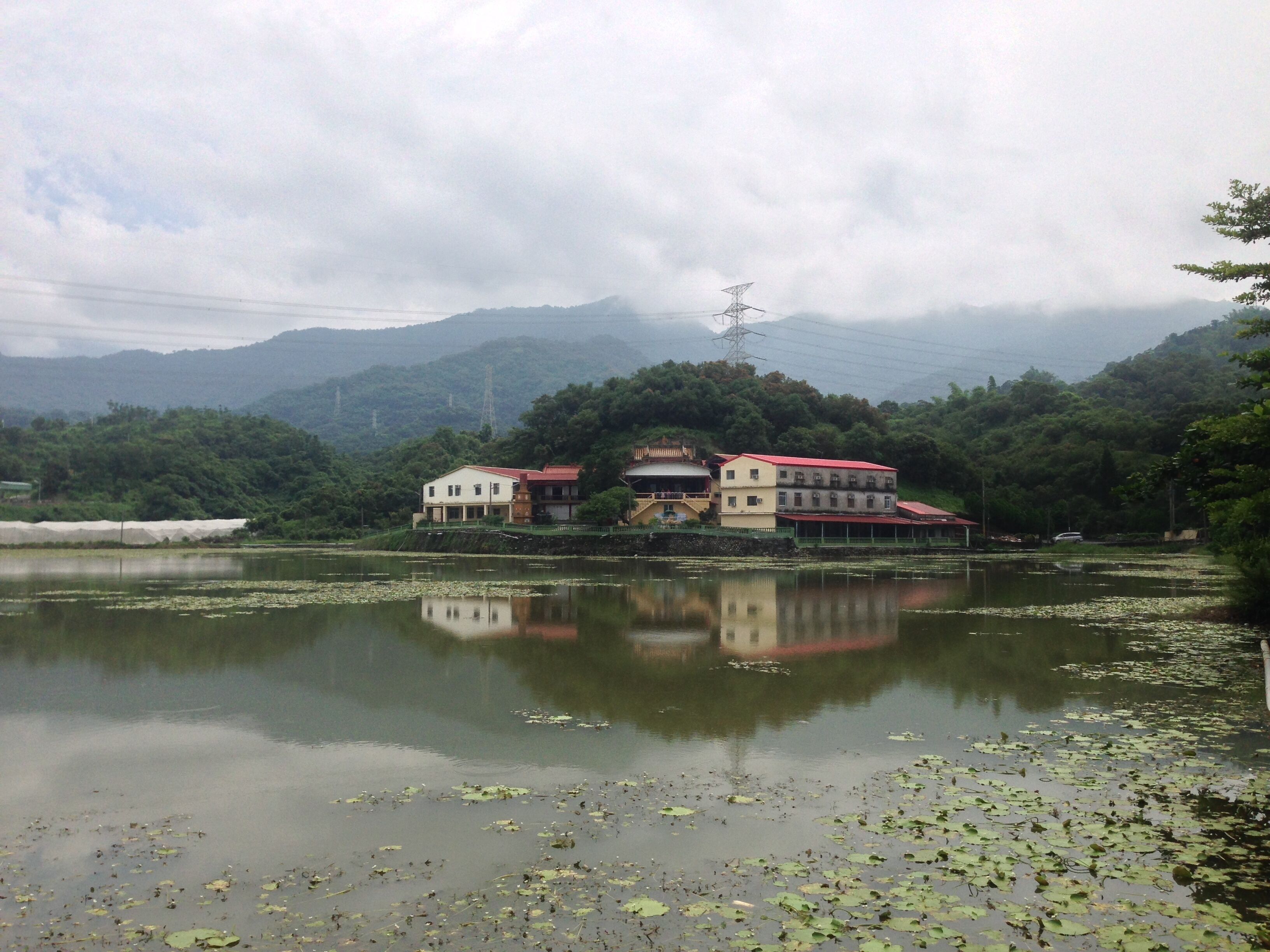 A lake with lily pads, a building with a red roof, and mountains in the background.