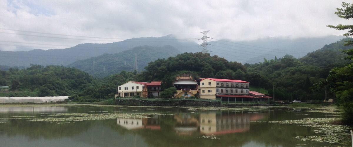 A lake with lily pads, a building with a red roof, and mountains in the background.