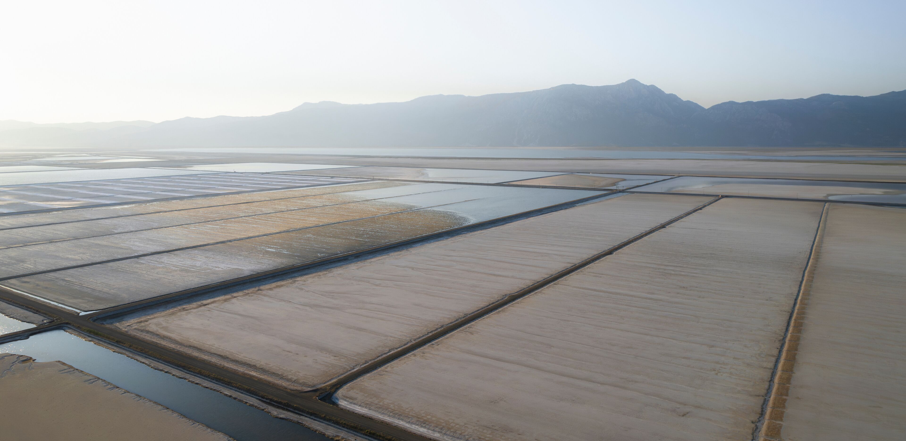 A salt flat with rectangular pools of water and distant mountains.