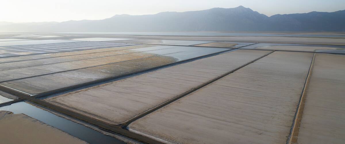 A salt flat with rectangular pools of water and distant mountains.