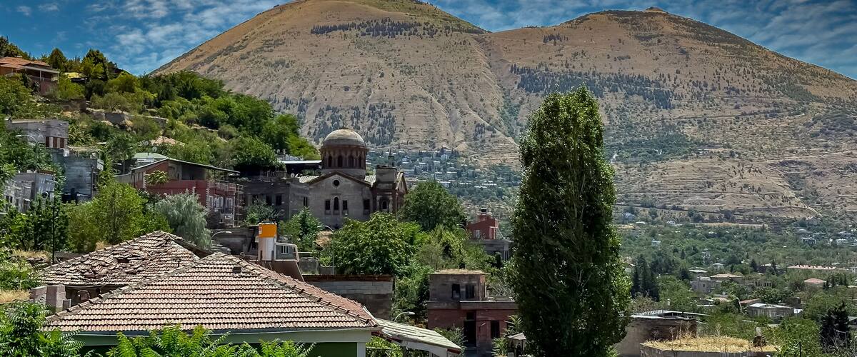 A mountainous landscape with a church, residential buildings, and lush greenery.