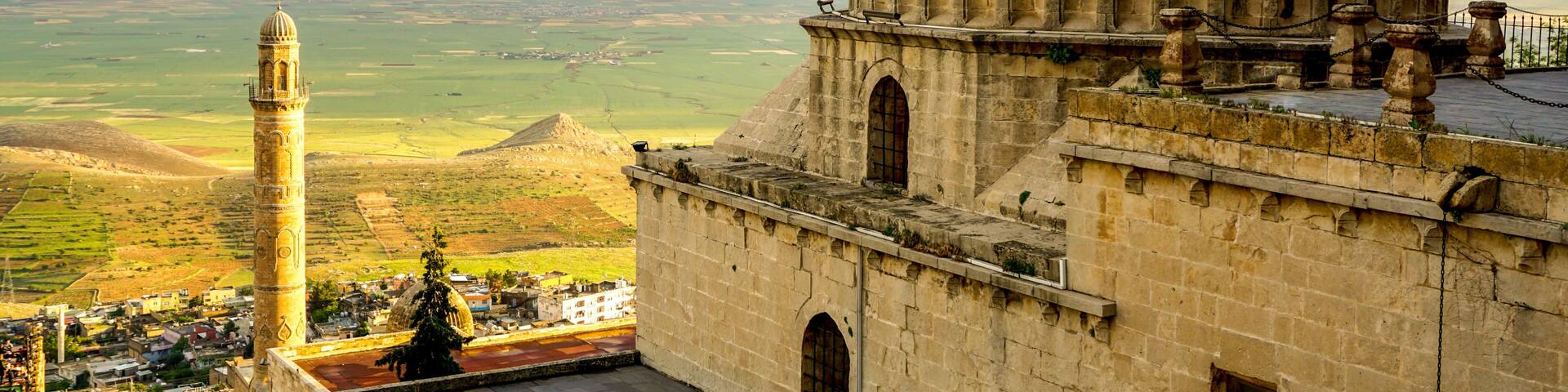 A historic building with a large dome and a minaret, overlooking a valley.