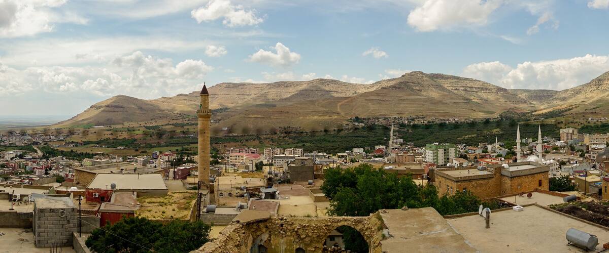 A cityscape with a prominent minaret, surrounded by mountains and a clear sky.