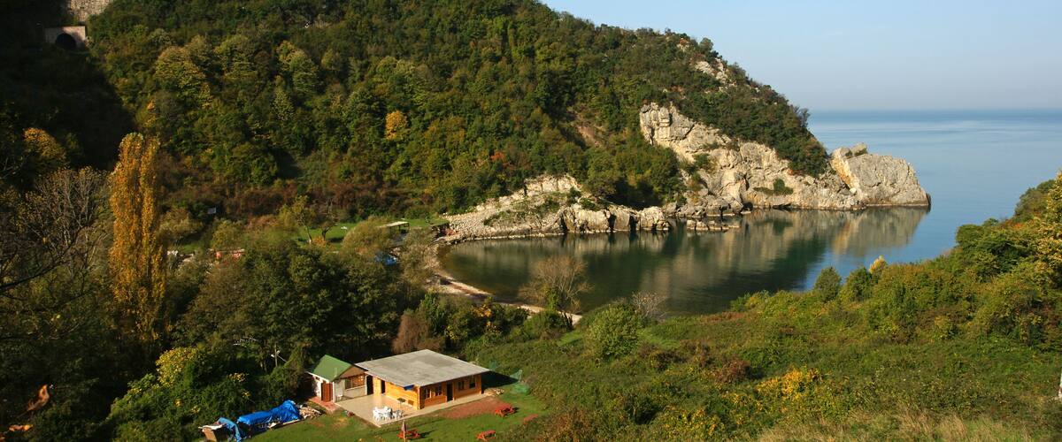 A coastal landscape with a house on a grassy hill, a rocky cliff, and a calm sea.