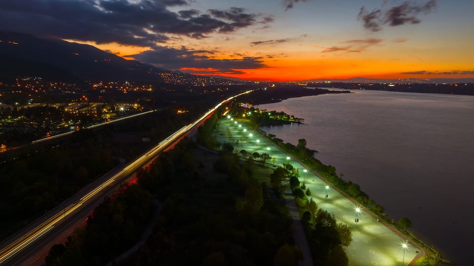 A cityscape at dusk with a river, a bridge, and a highway.