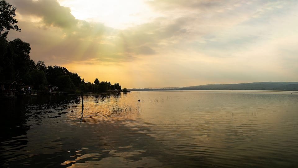 A calm lake with reflections of trees and a distant bridge.