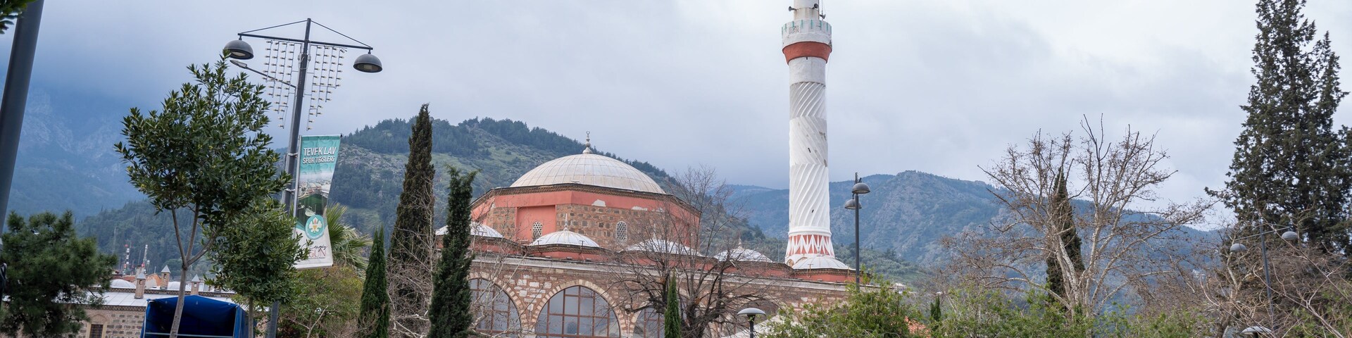 Una mezquita con un minarete alto y una cúpula, rodeada de vegetación y un telón de fondo montañoso.