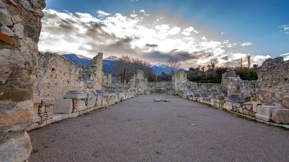 Ancient ruins with stone columns and a mountainous backdrop.