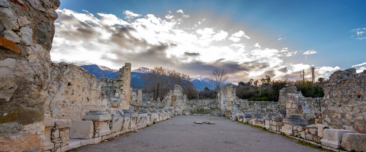Ancient ruins with stone columns and a mountainous backdrop.