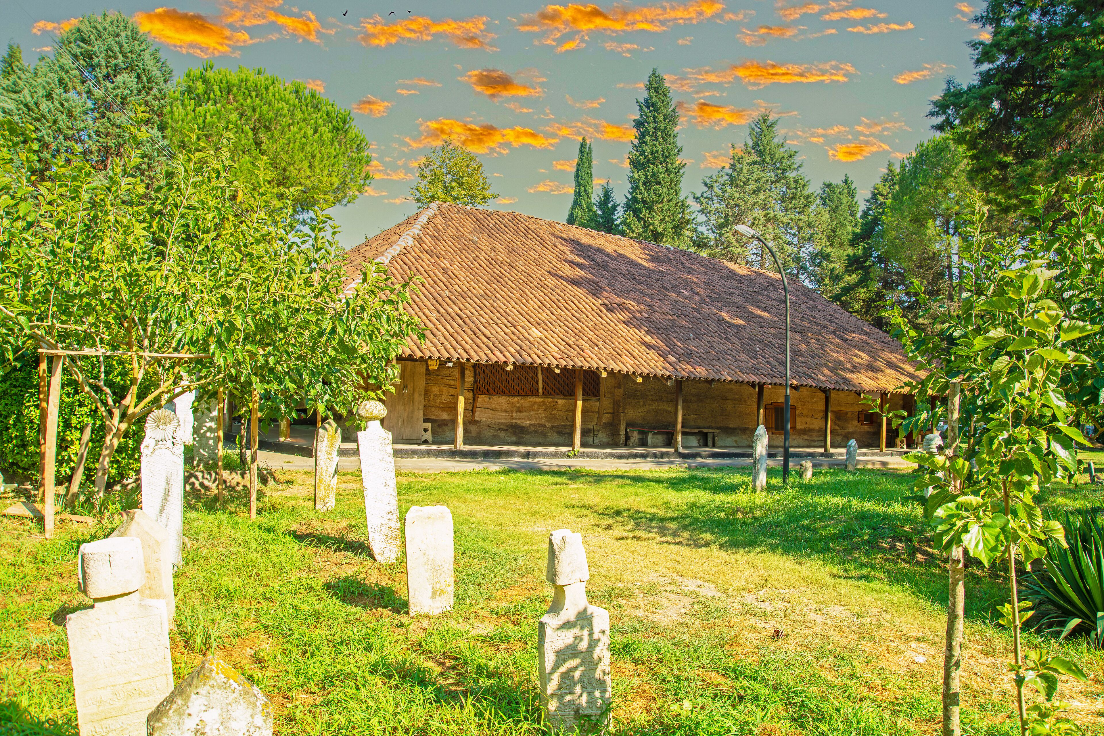 A rustic building with a tiled roof surrounded by lush greenery and gravestones.