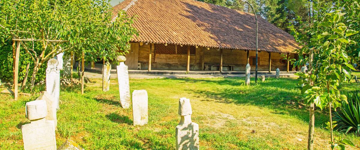 A rustic building with a tiled roof surrounded by lush greenery and gravestones.