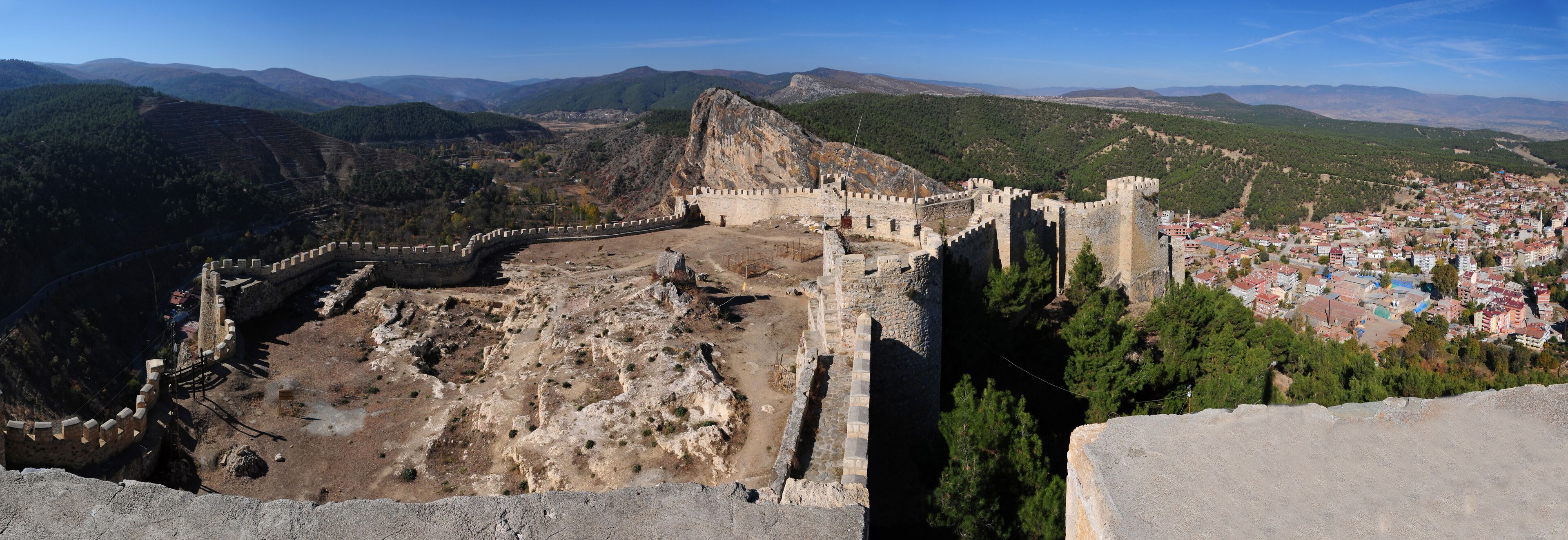 A historical fortress overlooking a town with a mountainous backdrop.