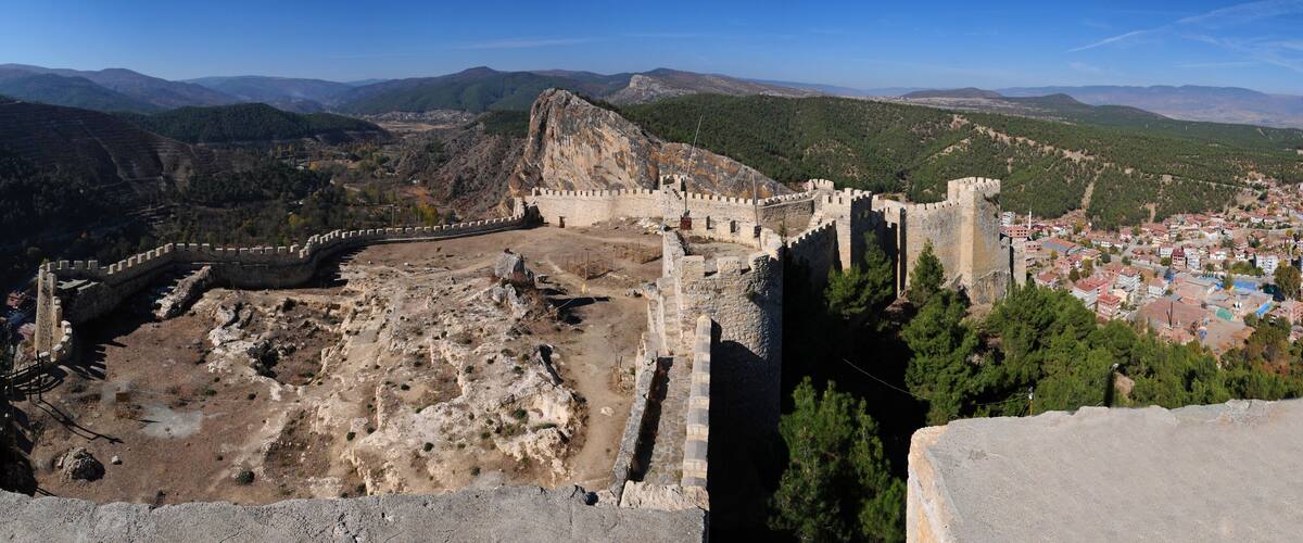 A historical fortress overlooking a town with a mountainous backdrop.