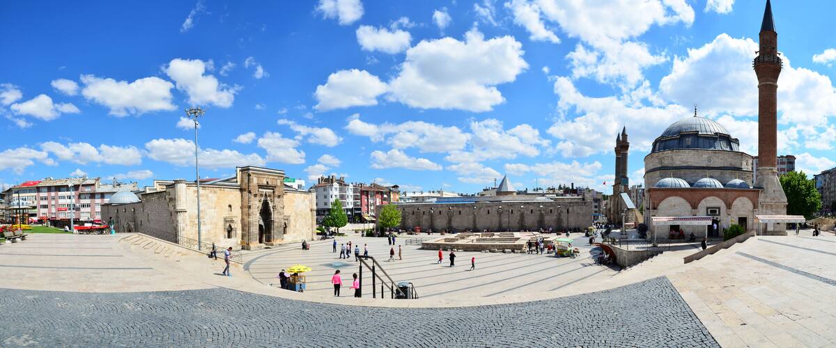 A historic square with a prominent mosque featuring a tall minaret and a dome, surrounded by stone buildings and cobblestone streets.