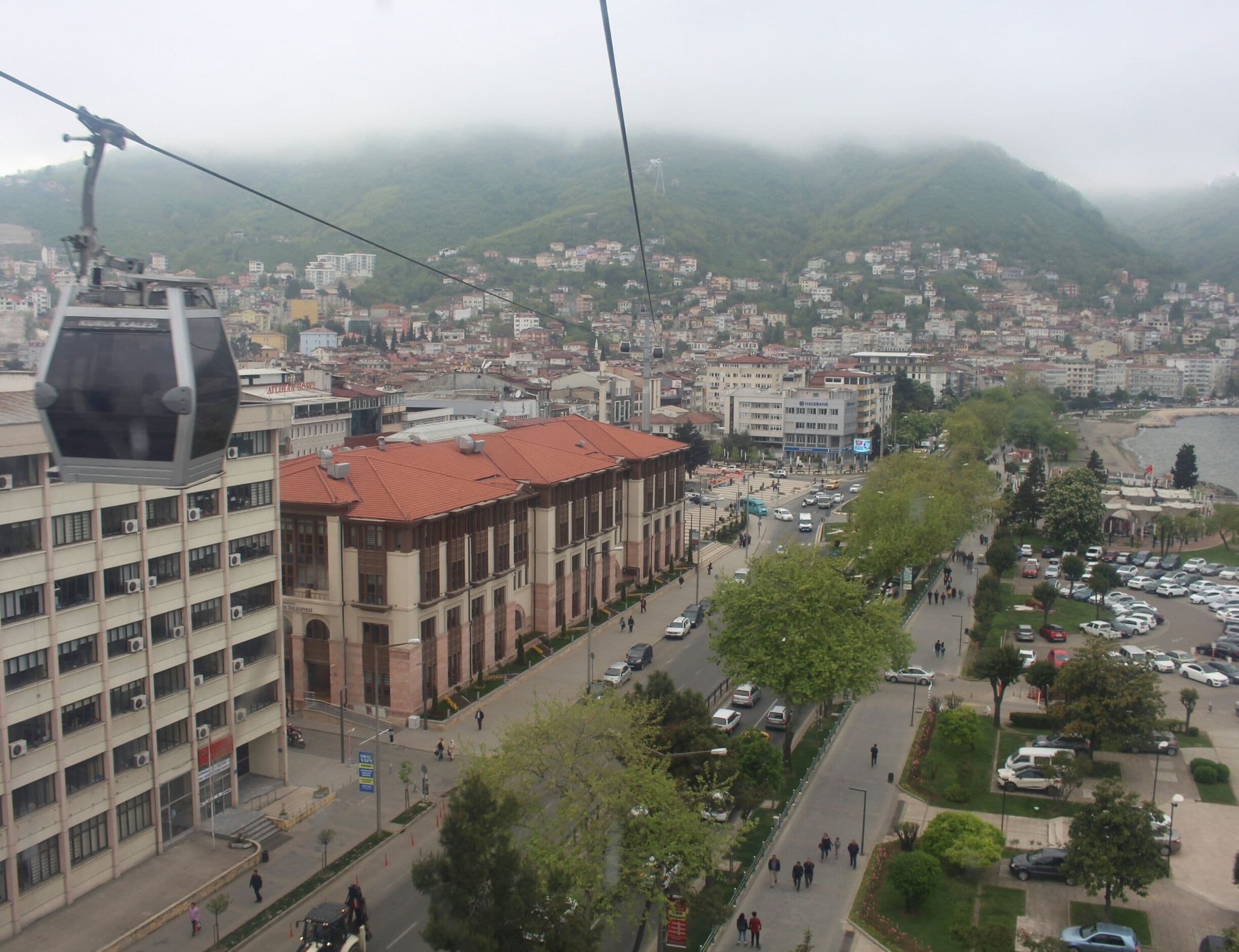 A cable car system, a cityscape with buildings, a river, and a mountainous backdrop.