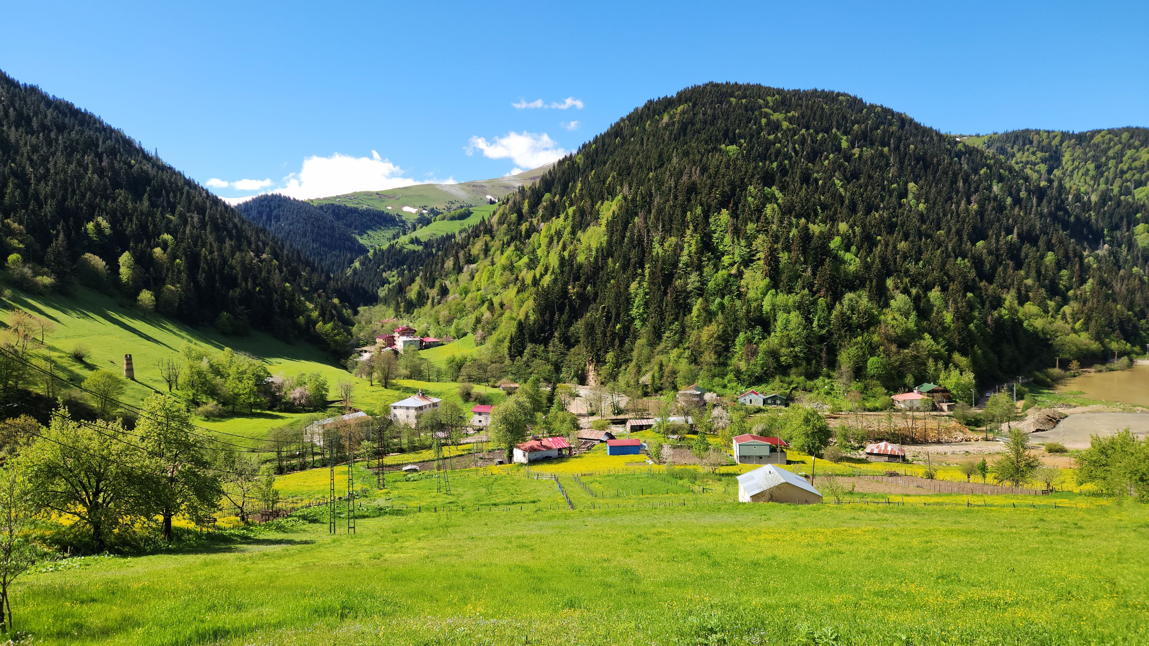 Ländliche Landschaft mit sanften Hügeln, einem Fluss und verstreuten Häusern.