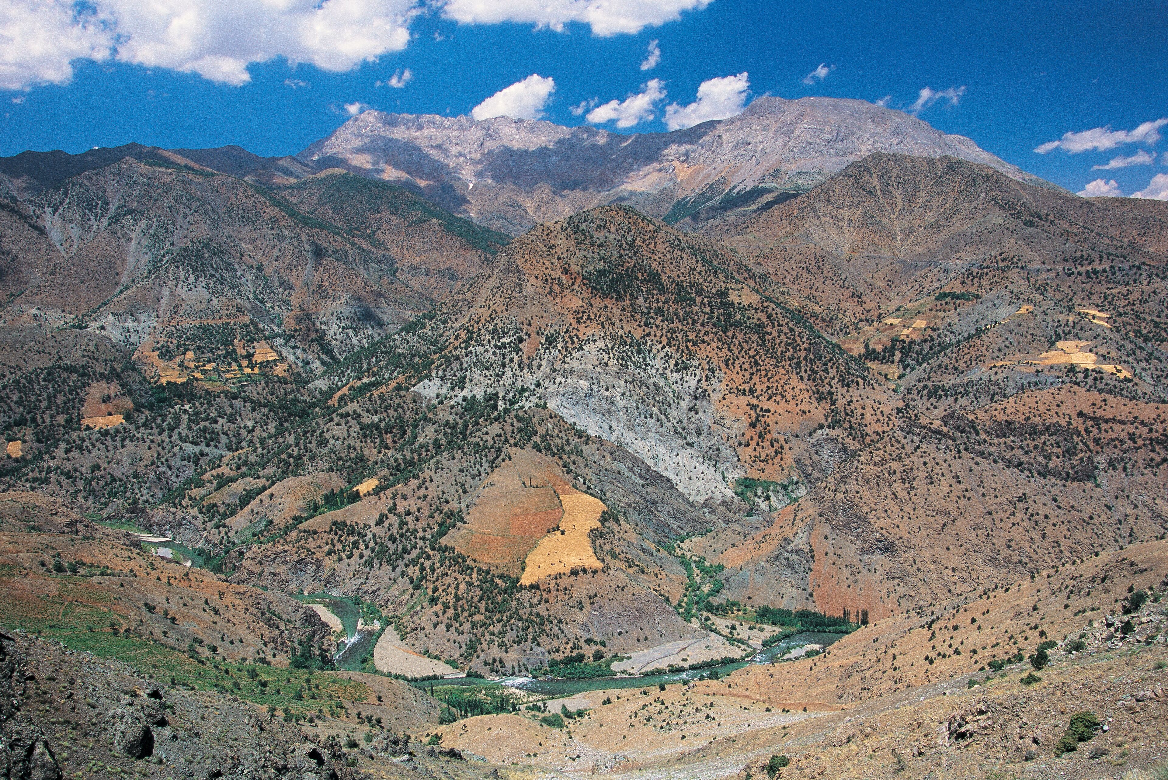 A mountainous landscape with a river flowing through a valley, surrounded by rugged terrain and sparse vegetation.