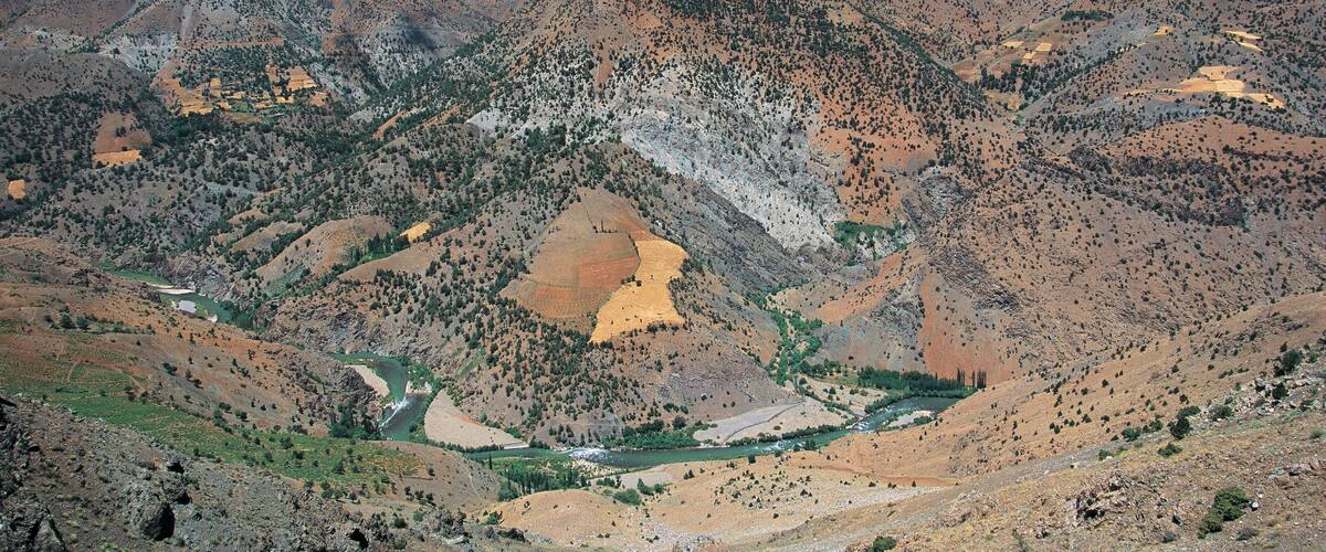 A mountainous landscape with a river flowing through a valley, surrounded by rugged terrain and sparse vegetation.